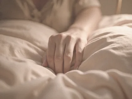 Una mano en reposo sobre una almohada de lino, con luz cálida de noche.